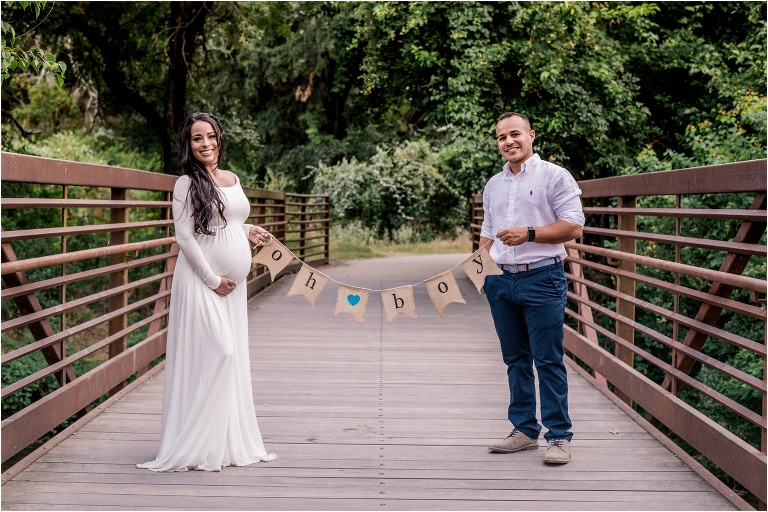 Couple on bridge during maternity photoshoot in Cedar Park Texas holding boy banner