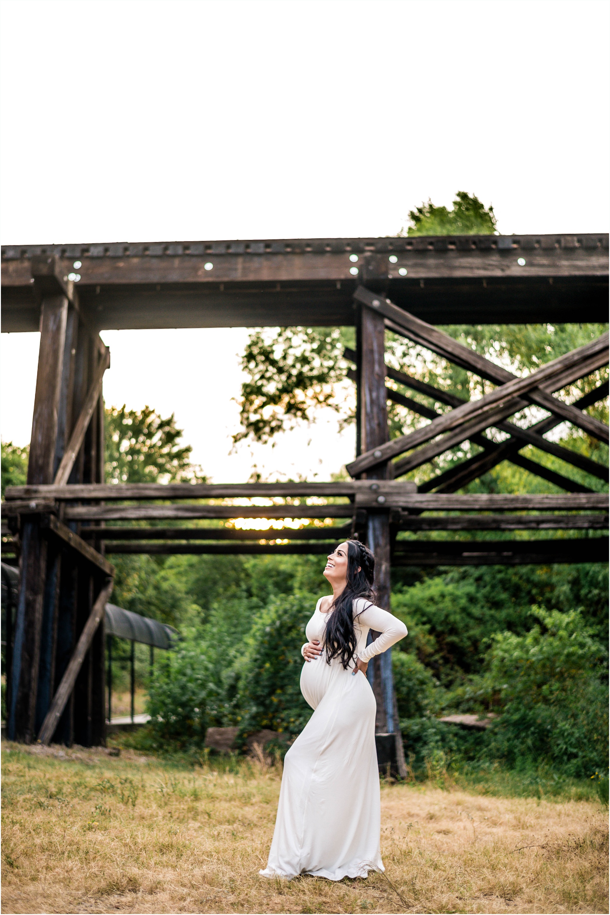 Beautiful expecting mother at sunset golden hour by bridge in Cedar Park Texas in white maxi dress maternity photographer