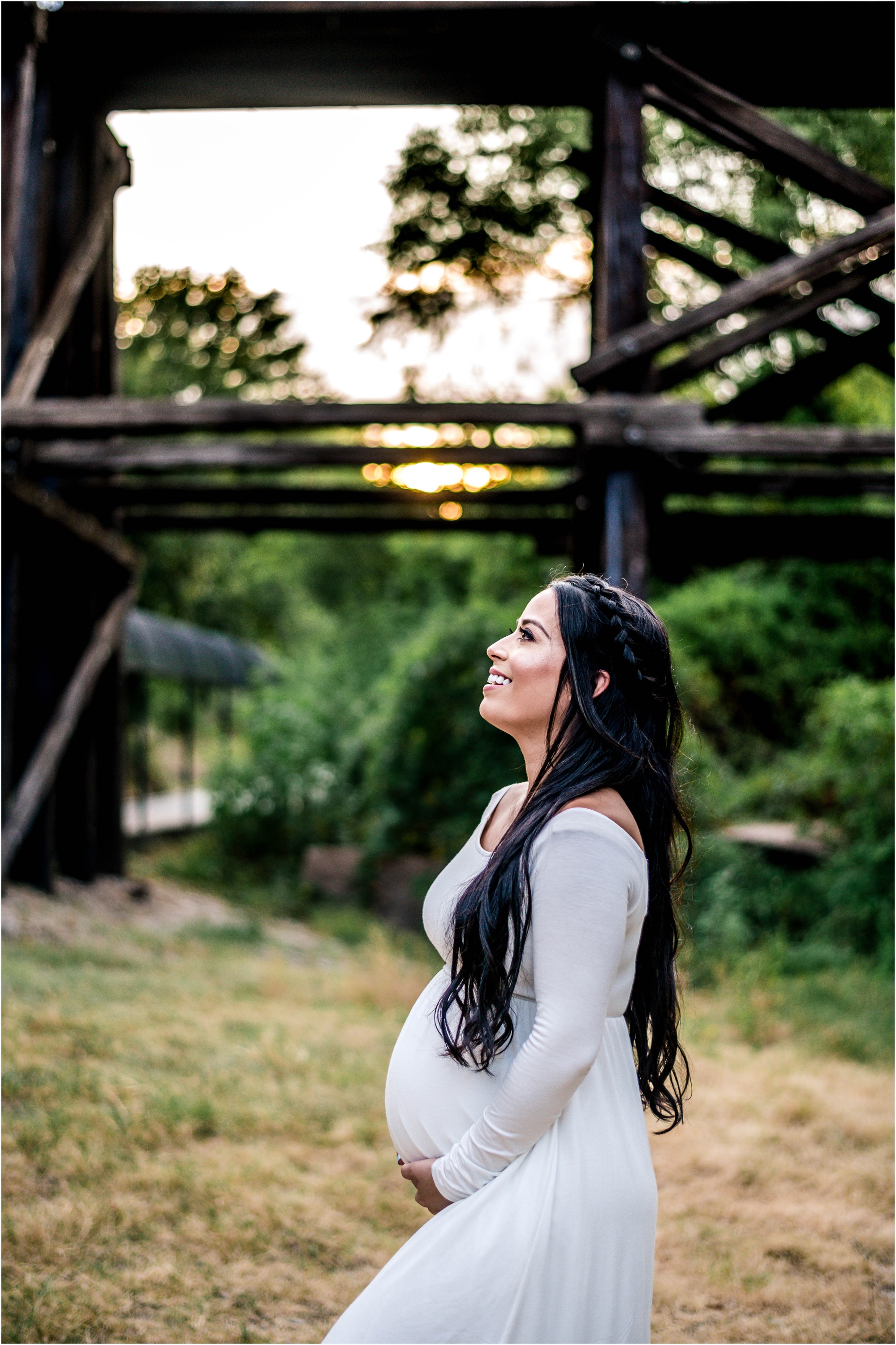 Beautiful expecting mother at sunset golden hour by bridge in Cedar Park Texas in white maxi dress maternity photographer