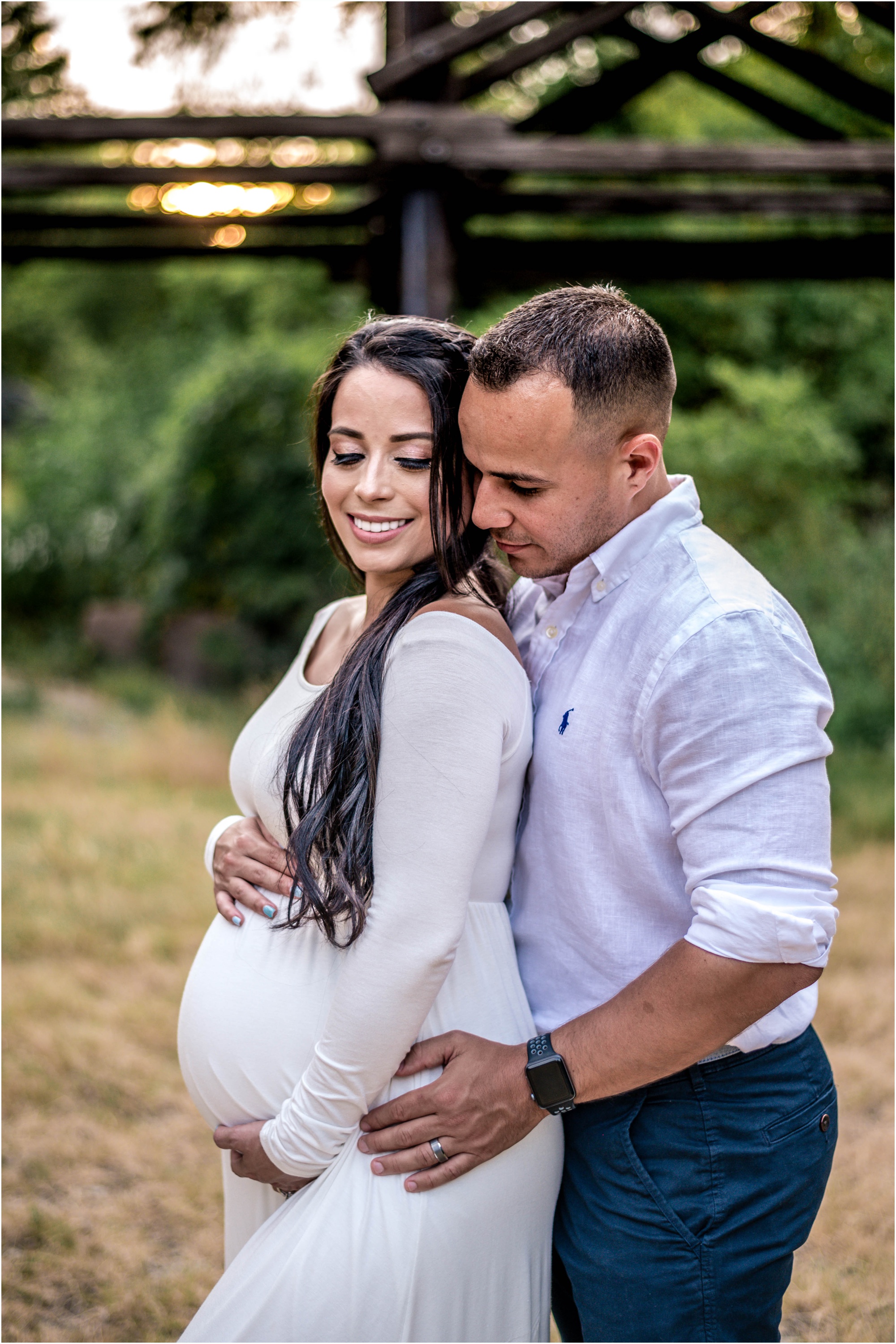Beautiful couple during maternity photoshoot at sunset golden hour by bridge in Cedar Park Texas in white maxi dress natural light family photographer