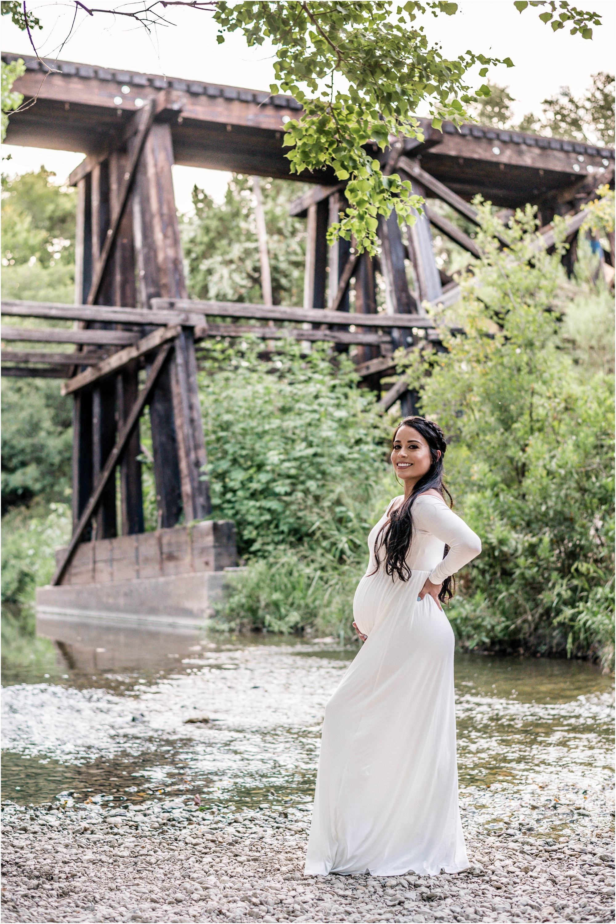 Beautiful expecting mother at sunset golden hour by bridge in Cedar Park Texas in white maxi dress maternity photographer