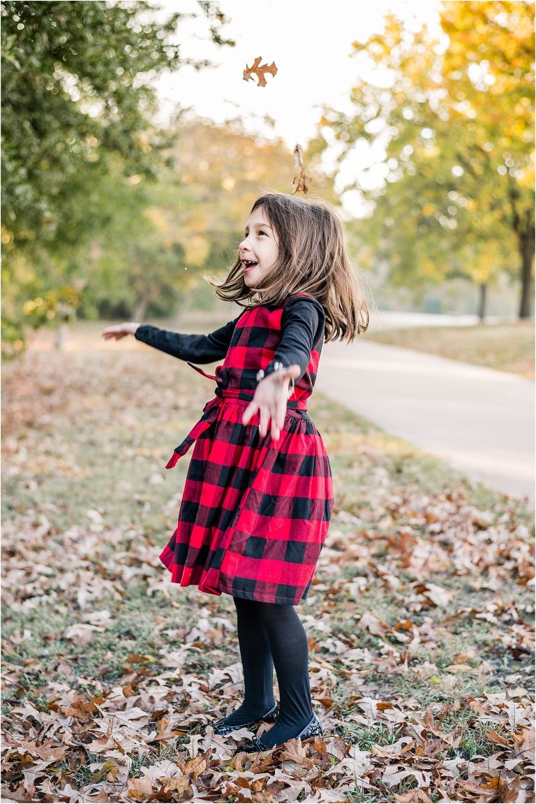 Little girl playing in leaves in Pflugerville Texas during family photoshoot by natural light portrait photographer